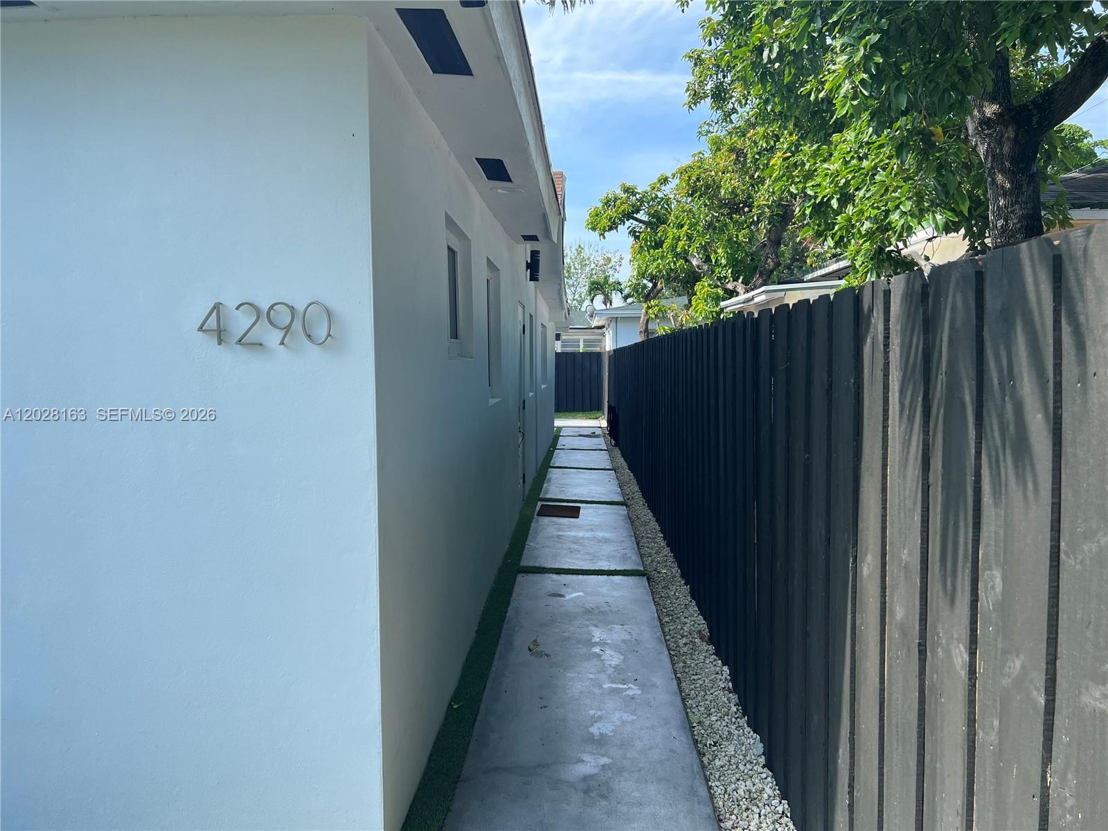 A narrow concrete walkway runs between a white building wall and a tall black fence — 4290 SW 9th St # B, Miami FL 33134, MIAMI, FL