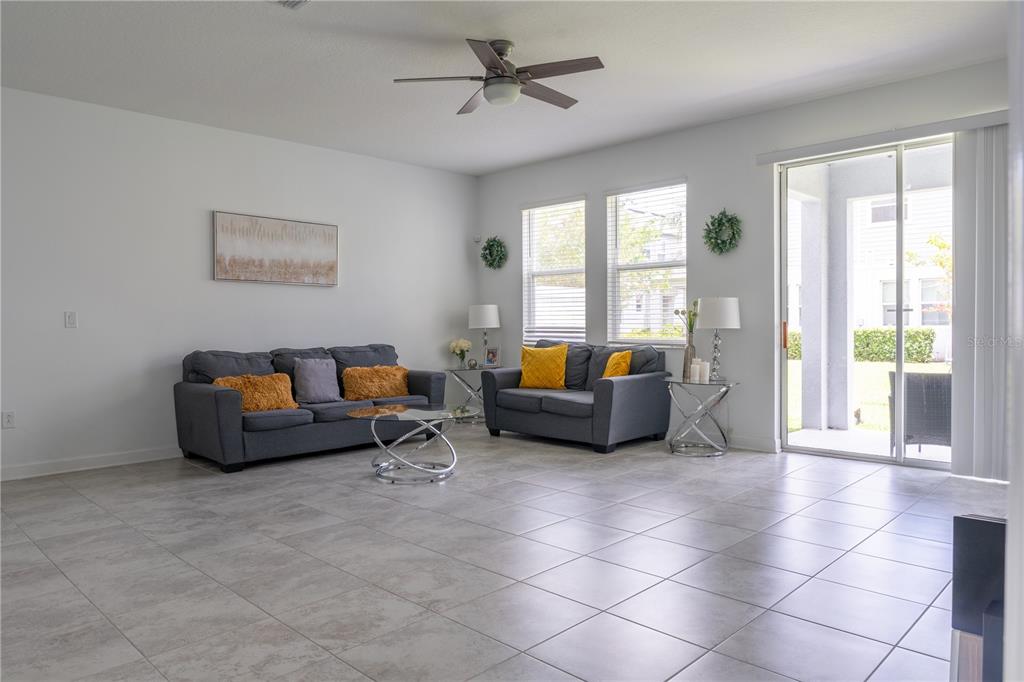 A living room features gray sofas, tile flooring, a ceiling fan, and a sliding glass door — 12109 SCRUB PALM LANE, ORLANDO, FL