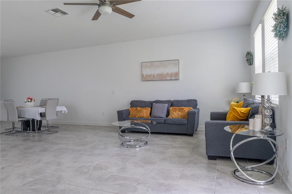 A living room with gray sofas, a glass coffee table, and an adjacent dining area — 12109 SCRUB PALM LANE, ORLANDO, FL