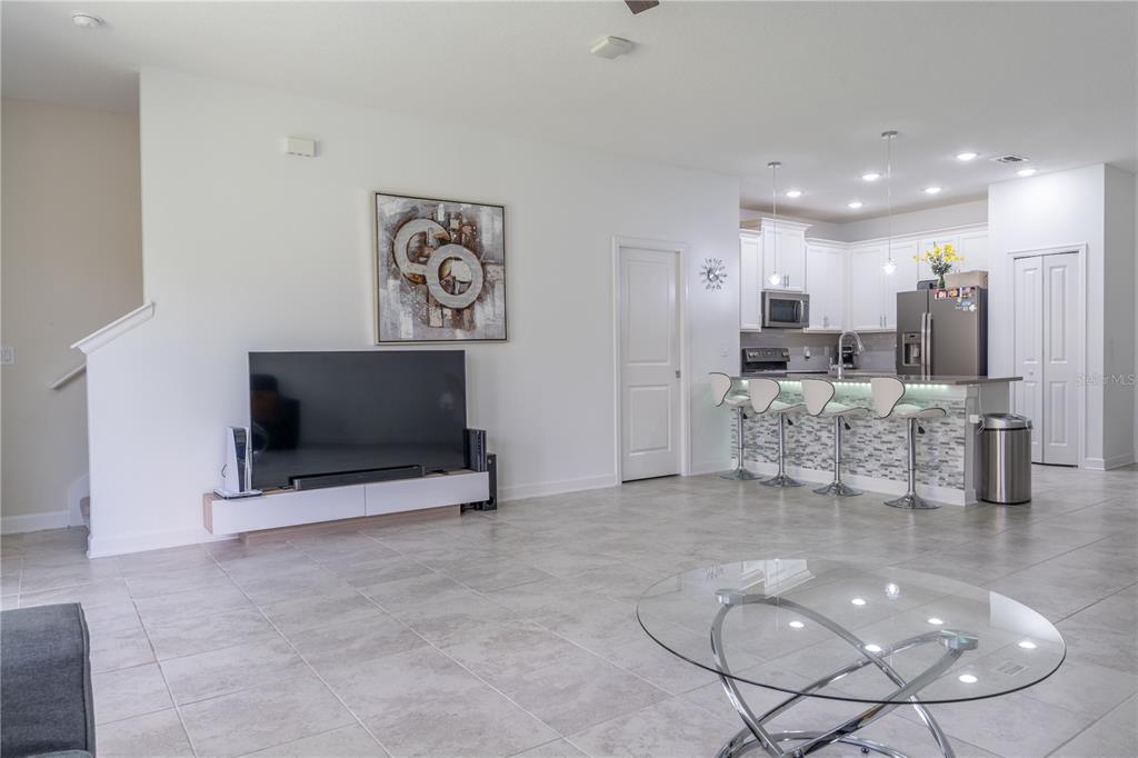 An open-concept living room features tile flooring, a wall-mounted television, and a kitchen island — 12109 SCRUB PALM LANE, ORLANDO, FL