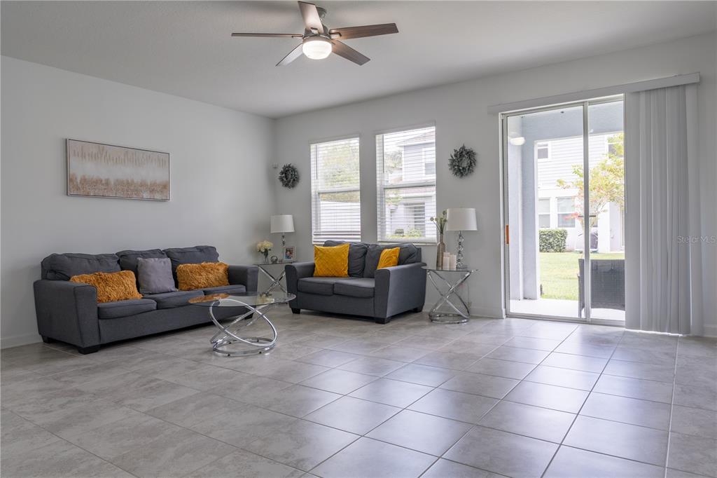 A living room features gray sofas, a glass coffee table, tile flooring, and sliding glass doors — 12109 SCRUB PALM LANE, ORLANDO, FL