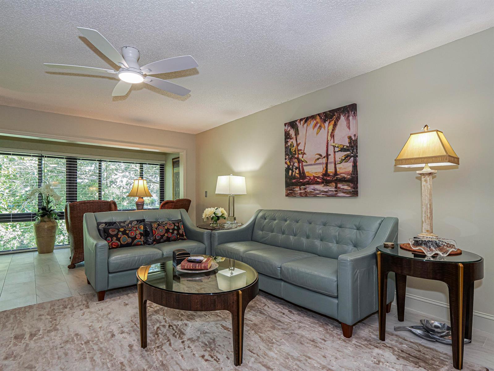 A living room features two blue leather sofas, a glass coffee table, and palm tree art — 400 18th Street # G5, Vero Beach FL 32960, VERO BEACH, FL