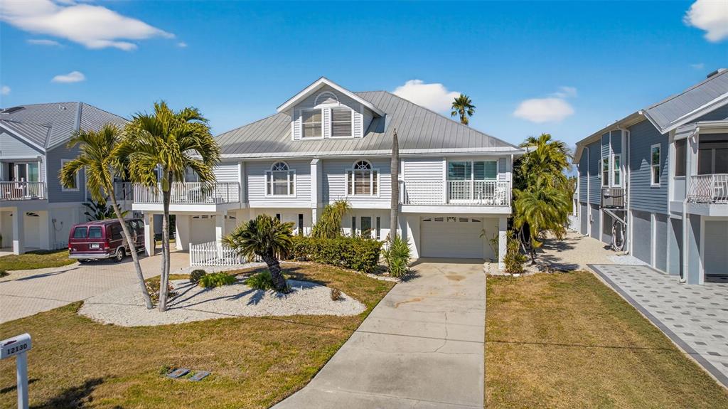 A two-story house with light gray siding, a metal roof, and a concrete driveway — 12130 SIESTA DRIVE, FORT MYERS BEACH, FL