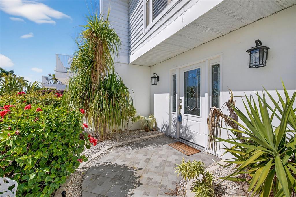 A white front door with a glass insert sits on a paved patio with landscaping — 12130 SIESTA DRIVE, FORT MYERS BEACH, FL