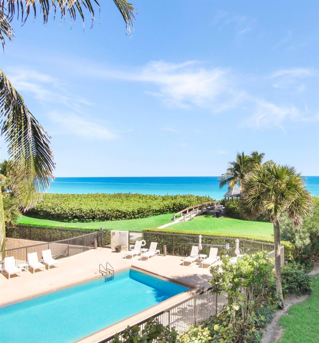 An outdoor swimming pool sits in front of a grassy lawn leading to the ocean — 420 Celestial Way # 202, Juno Beach FL 33408, JUNO BEACH, FL