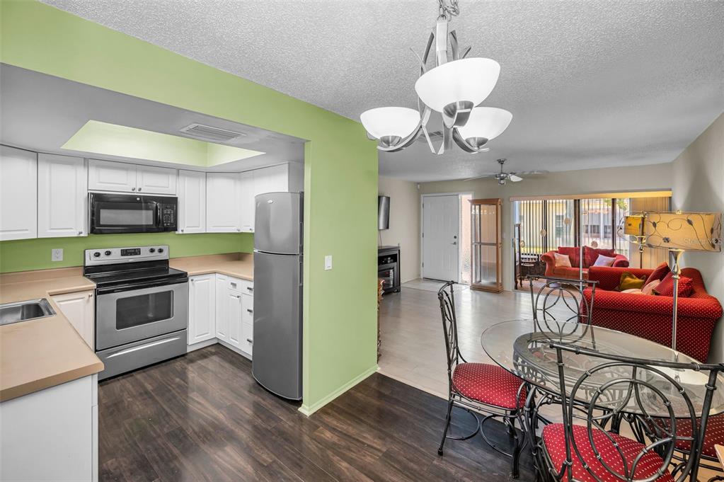 A kitchen with white cabinets and stainless appliances opens into a dining and living area — 1121 QUEEN ANNE DRIVE UNIT C, PALM HARBOR, FL
