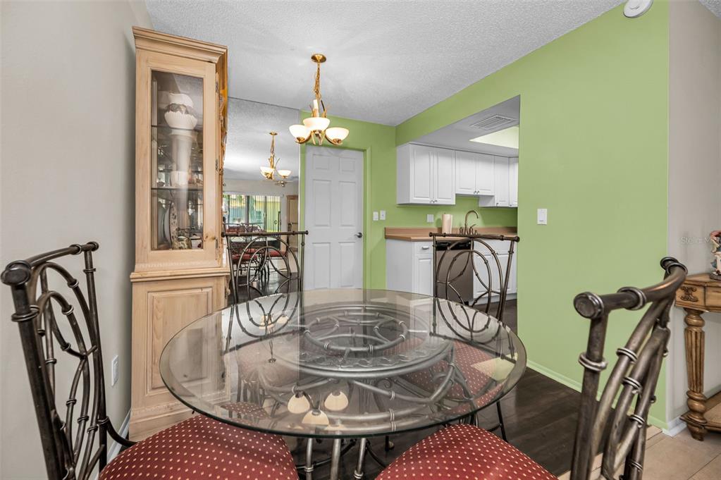 A dining area with a glass-topped table and metal chairs sits before a green-walled kitchen — 1121 QUEEN ANNE DRIVE UNIT C, PALM HARBOR, FL