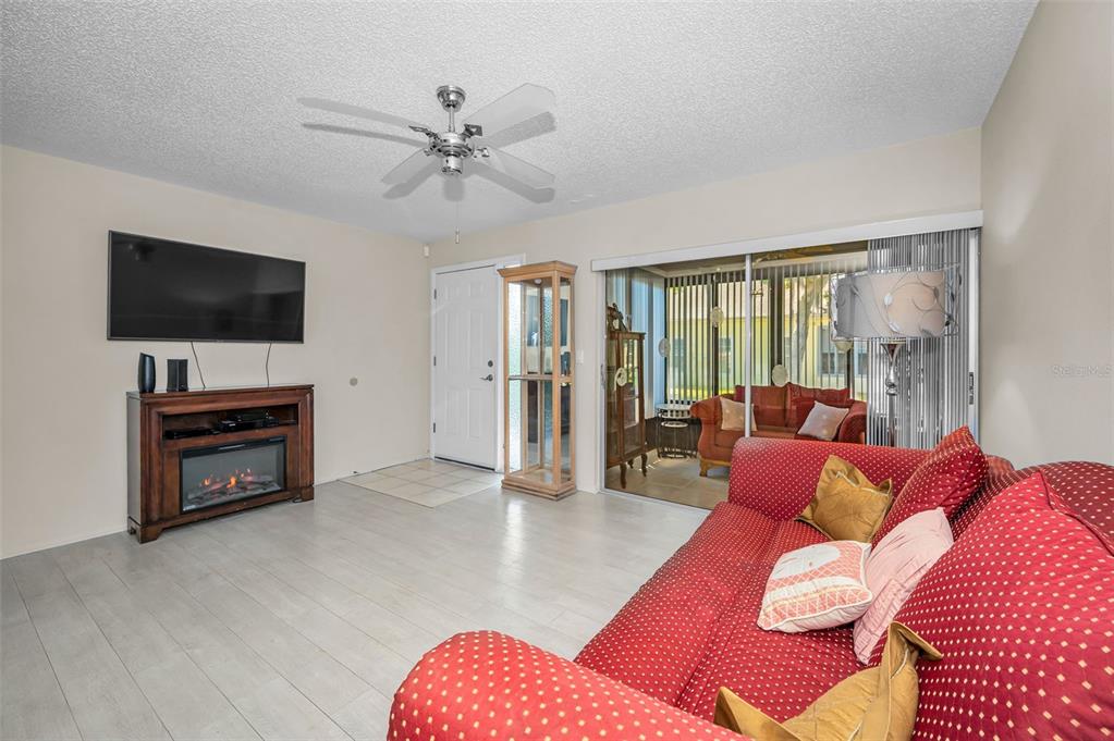 A living room with light wood floors, a red patterned sofa, and an electric fireplace — 1121 QUEEN ANNE DRIVE UNIT C, PALM HARBOR, FL