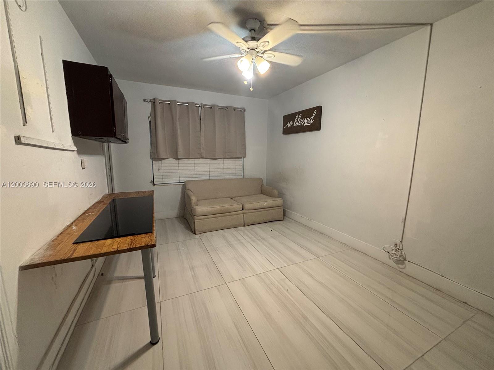 A small room features white tile flooring, a beige loveseat, and a wooden desk — 250 SE Park St # 3, Dania Beach FL 33004, DANIA BEACH, FL