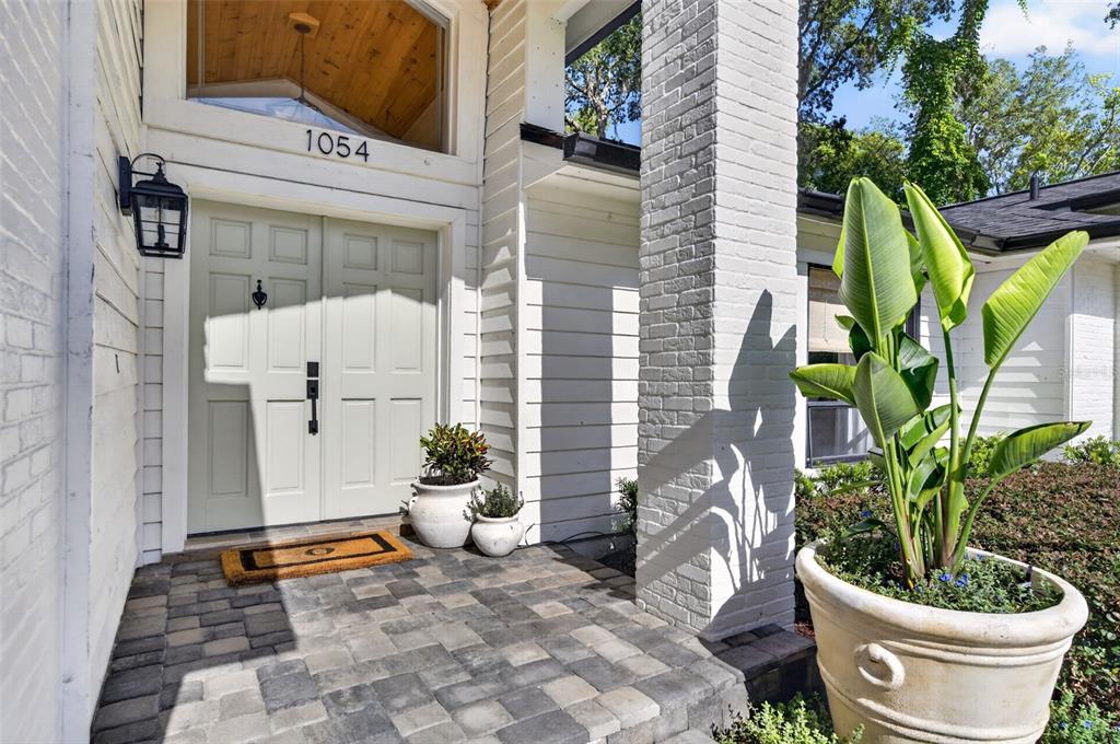 The exterior of a white brick house features a wooden gabled entryway and paved walkway — 1054 WHISPERING COVE, CASSELBERRY, FL