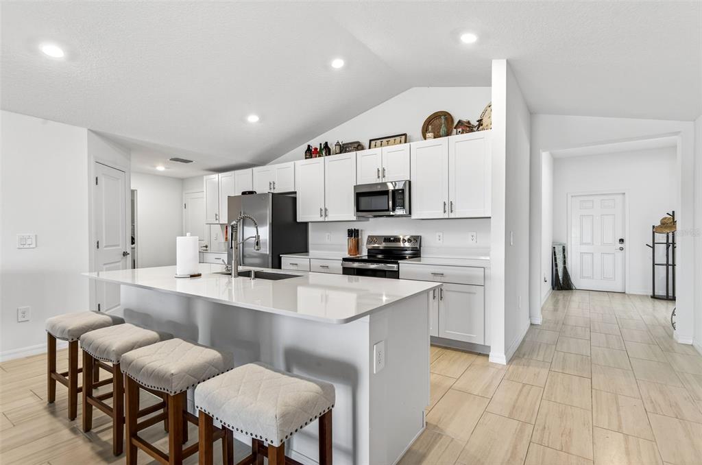 A modern kitchen features white cabinetry, a large island with bar seating, and tile flooring — 15217 ZIRCON RED DRIVE, WIMAUMA, FL