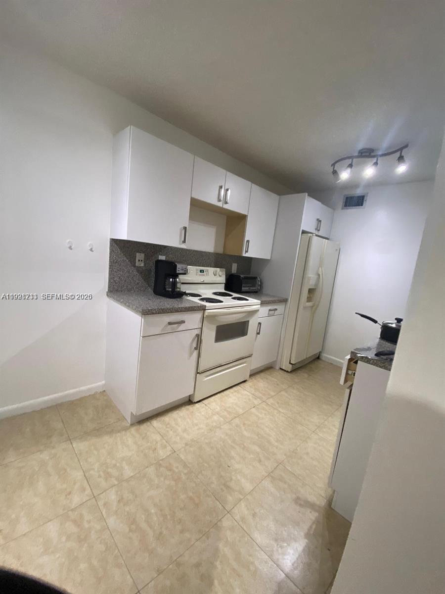 A kitchen features white cabinets, a white stove, a white refrigerator, and tiled flooring — 9761 NW 46th Ter # 107, Doral FL 33178, DORAL, FL