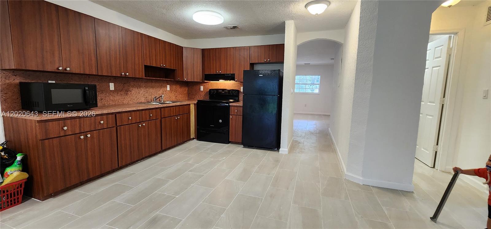A kitchen features wood-toned cabinets, black appliances, and light-colored tile flooring — 10380 NW 10th Ave # 10380, Miami FL 33150, MIAMI, FL