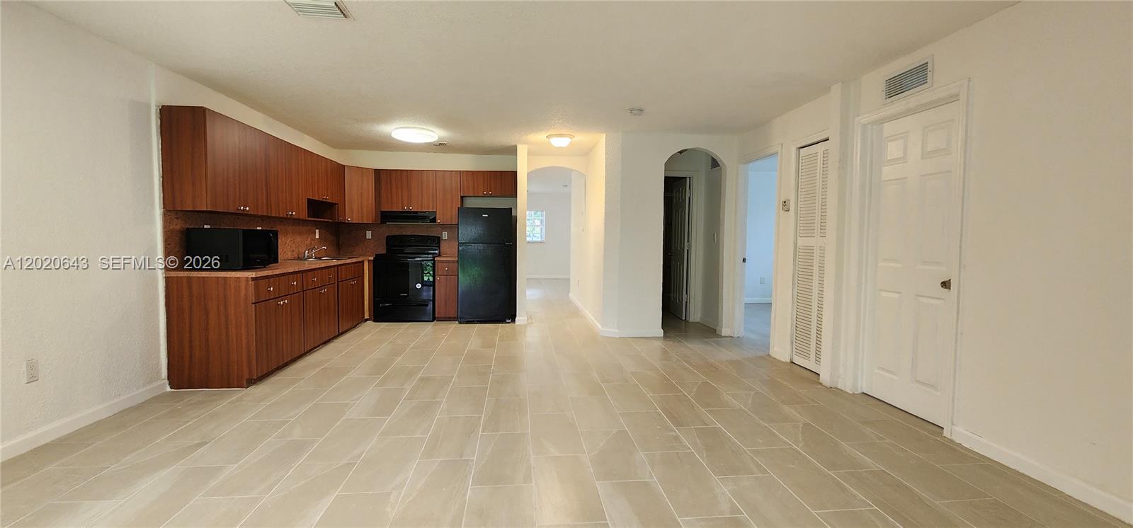 A kitchen with wood cabinets, black appliances, and light tile flooring opens to a hallway — 10380 NW 10th Ave # 10380, Miami FL 33150, MIAMI, FL