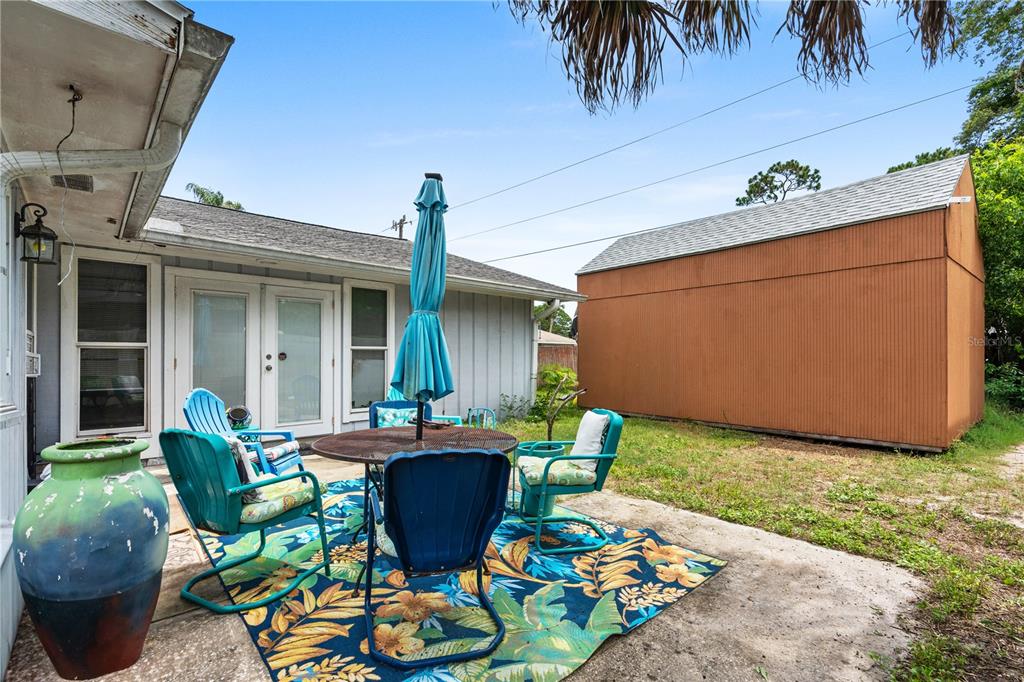 A patio with a table, chairs, and umbrella sits beside a house and a shed — 1945 FERN PALM DRIVE, EDGEWATER, FL