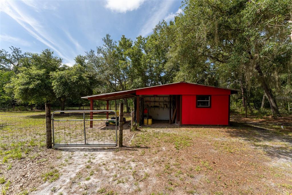A red shed with an attached open-sided shelter stands in a grassy, tree-filled yard — 14150 HIGHLAND ROAD, WIMAUMA, FL