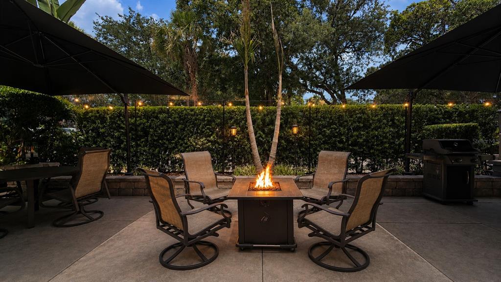 A patio features a fire pit surrounded by four chairs under two large black umbrellas — 233 STALLION LANE, RIVER RANCH, FL