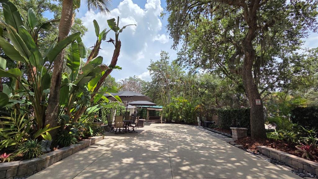 A paved patio area features outdoor seating under umbrellas, surrounded by lush landscaping and trees — 233 STALLION LANE, RIVER RANCH, FL