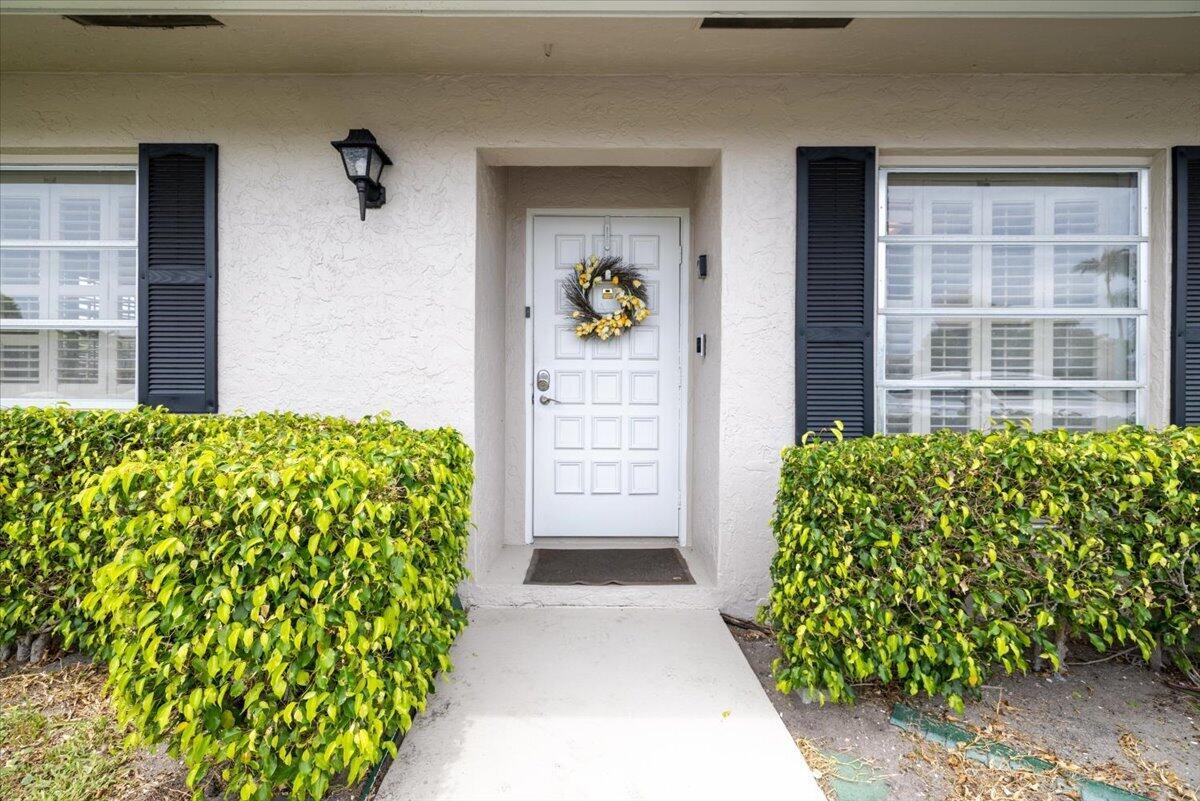 A white front door with a wreath is centered between two windows and manicured hedges — 1031 Citrus Way # a, Delray Beach FL 33445, DELRAY BEACH, FL