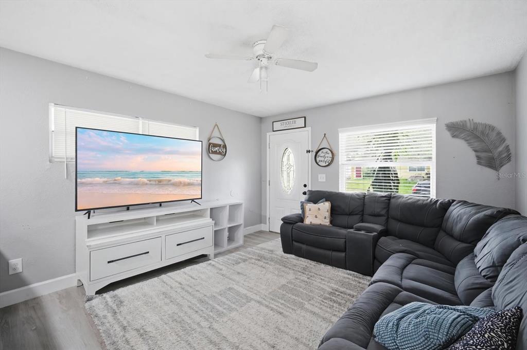 A living room features a large television, a white media console, and a dark sectional sofa — 7506 CORAL VINE LANE, TAMPA, FL