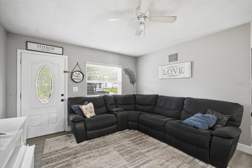 A living room features a large black sectional sofa, a textured area rug, and a front door — 7506 CORAL VINE LANE, TAMPA, FL
