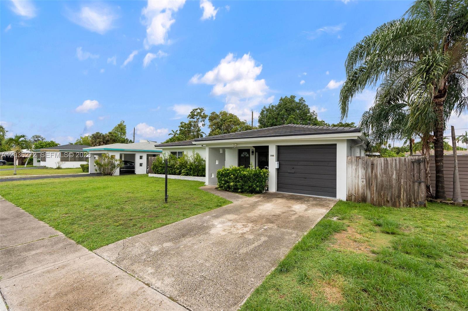 A single-story house with a white exterior, a dark garage door, and a concrete driveway — 706 N 32nd Ct, Hollywood FL 33021, HOLLYWOOD, FL