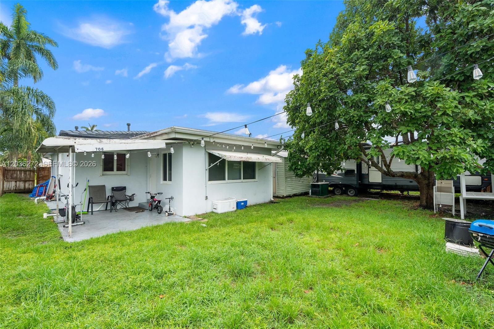 A white house exterior features a covered patio, string lights, and a large backyard tree — 706 N 32nd Ct, Hollywood FL 33021, HOLLYWOOD, FL
