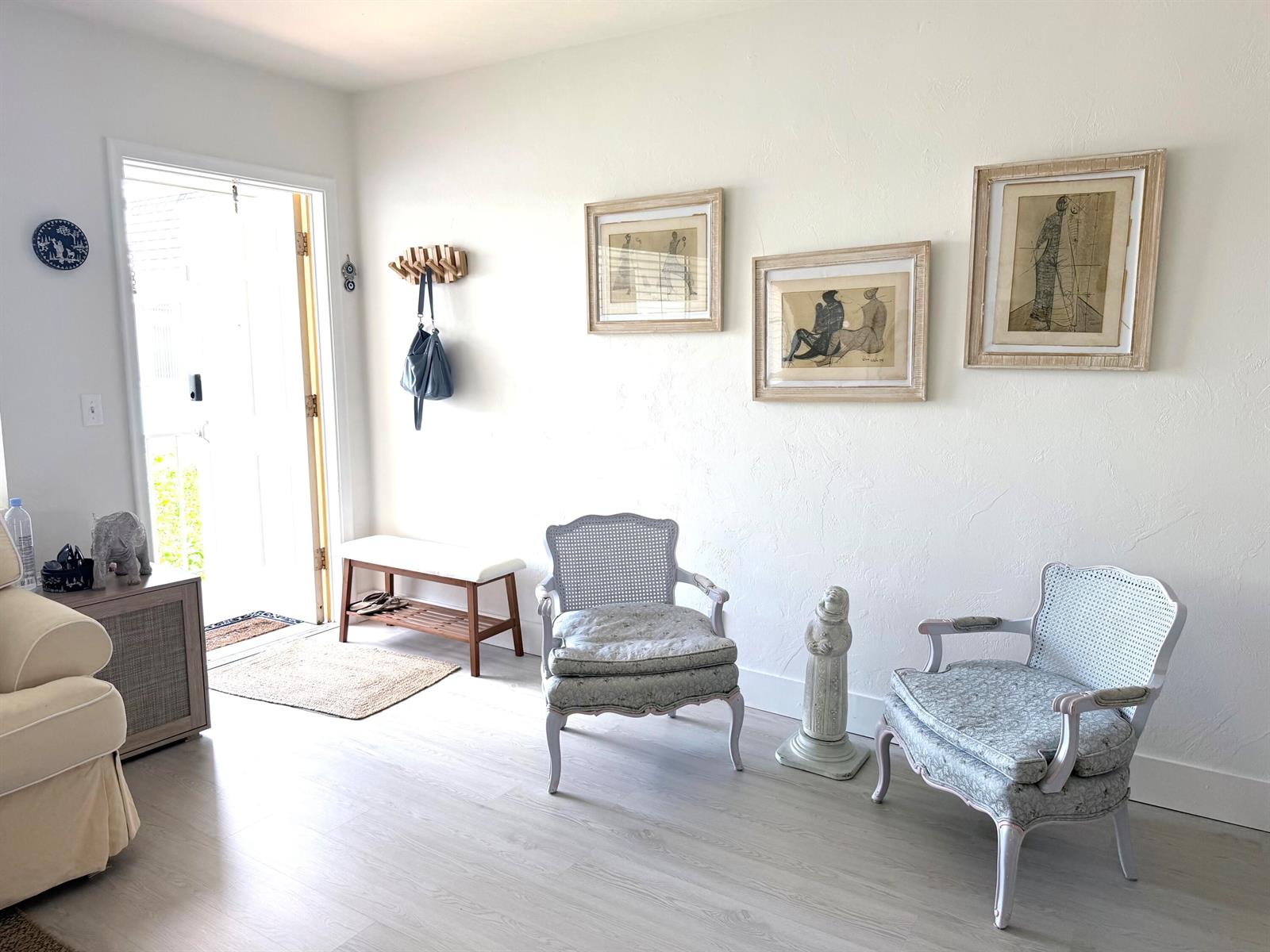 A bright entryway features light wood flooring, two patterned armchairs, a bench, and wall art — 3322 Cynthia Lane # 207, FL 33461, FL
