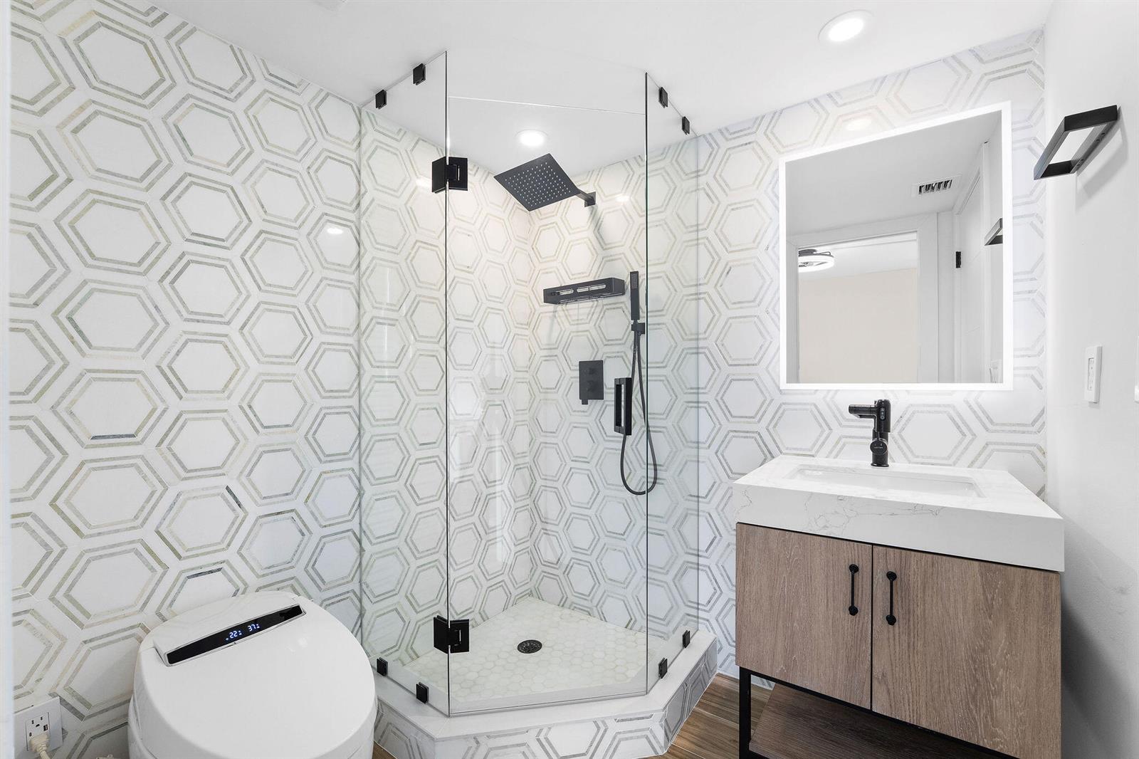 A modern bathroom features a glass-enclosed corner shower, a vanity, and geometric patterned wall tiles — 911 Ocean Drive # 201, Juno Beach FL 33408, JUNO BEACH, FL