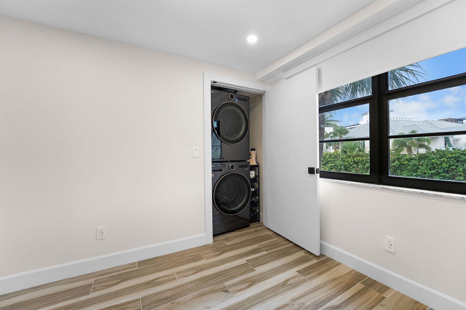A room with wood-look tile flooring features a stacked washer and dryer in a closet — 911 Ocean Drive # 201, Juno Beach FL 33408, JUNO BEACH, FL