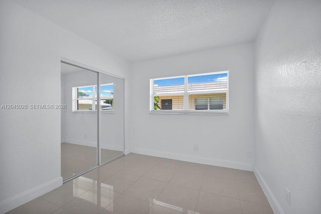 An empty bedroom features white walls, light-colored tile flooring, and a mirrored sliding closet door — 6890 SW 5th St, Margate FL 33068, MARGATE, FL