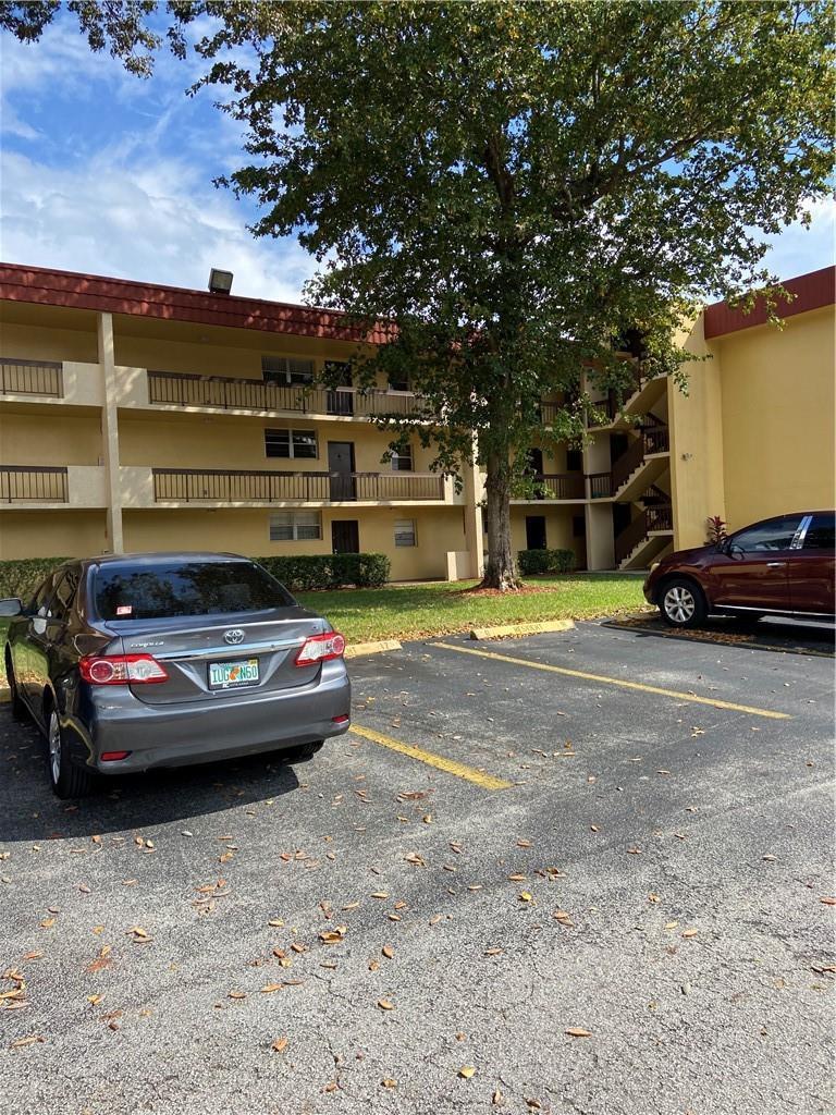 A multi-story apartment building exterior with a parking lot and a large tree in front — 3253 Foxcroft Road # G212, Miramar FL 33025, MIRAMAR, FL