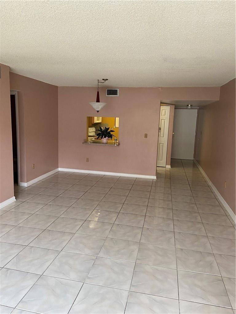 An empty living room with light-colored tile flooring, pink walls, and a kitchen pass-through window — 3253 Foxcroft Road # G212, Miramar FL 33025, MIRAMAR, FL