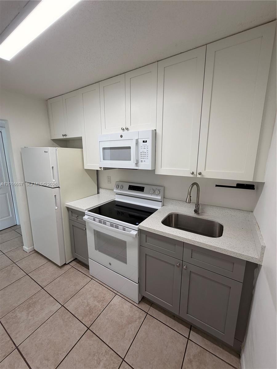 A small kitchen features white upper cabinets, gray lower cabinets, and white appliances — 6990 NW 186th St # 210A, Hialeah FL 33015, HIALEAH, FL
