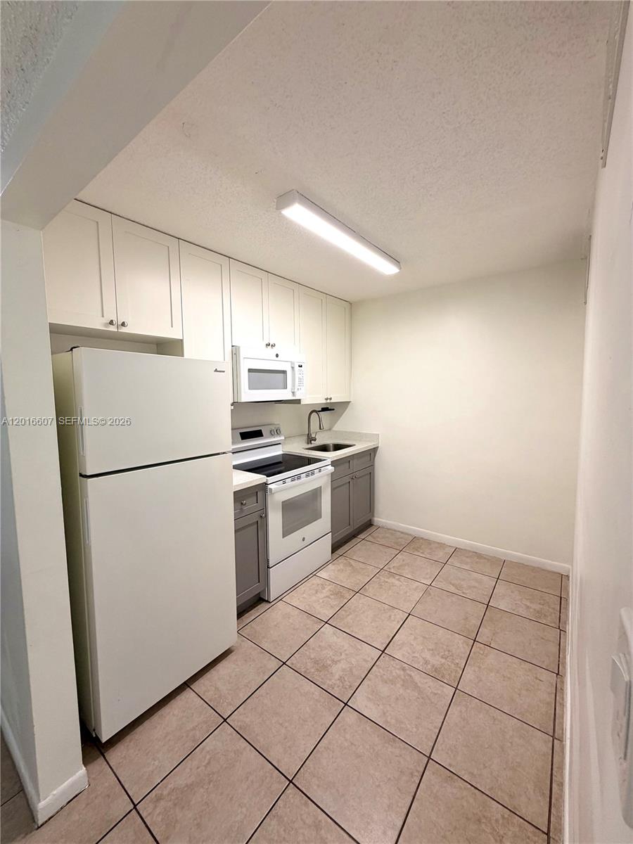 A small kitchen features white upper cabinets, gray lower cabinets, and a white refrigerator — 6990 NW 186th St # 210A, Hialeah FL 33015, HIALEAH, FL