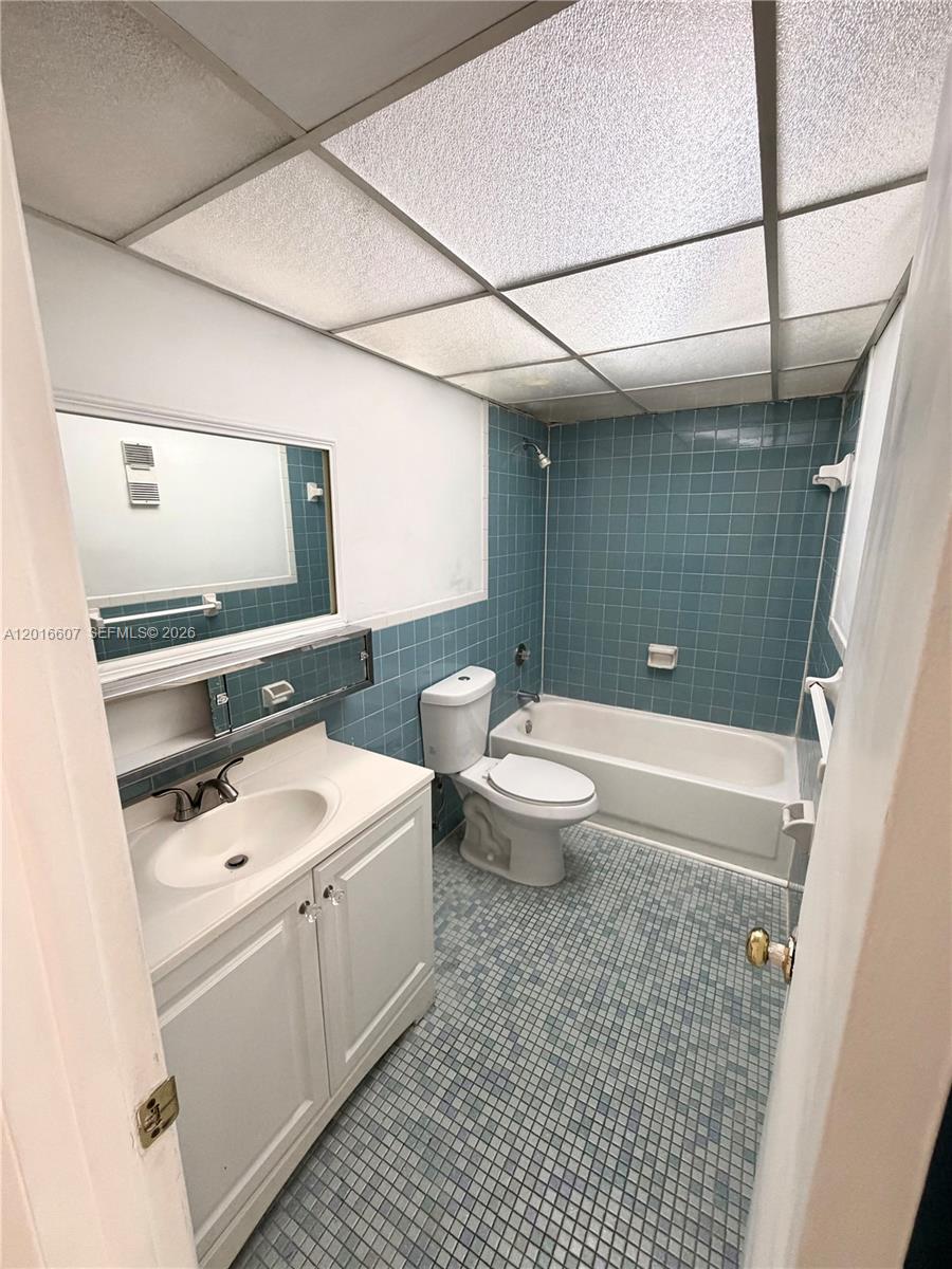 A bathroom features a white vanity, a toilet, and a bathtub with blue wall tiles — 6990 NW 186th St # 210A, Hialeah FL 33015, HIALEAH, FL