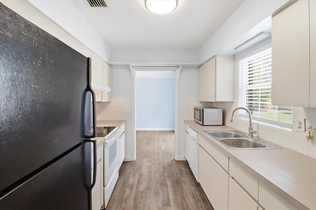 A galley kitchen features white cabinets, light countertops, a black refrigerator, and wood-look flooring — 9451 W GREEN BAY LANE, CRYSTAL RIVER, FL