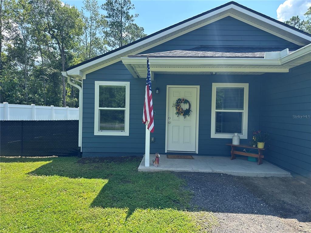 A blue-sided house features a front porch, a white door, and an American flag — 10010 MCMAHON AVENUE, HASTINGS, FL