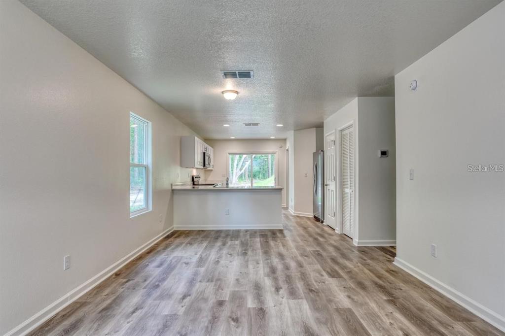 A kitchen with white cabinets and a breakfast bar overlooks a room with wood-look flooring — 10010 MCMAHON AVENUE, HASTINGS, FL