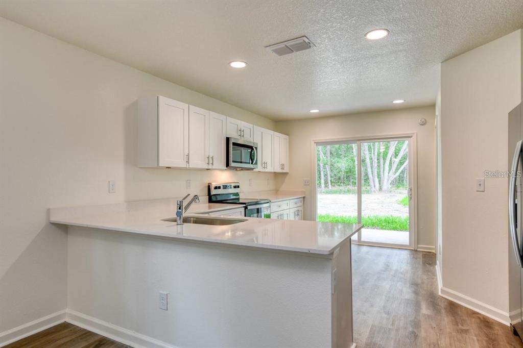 A kitchen with white cabinets, quartz countertops, and a sliding glass door to the backyard — 10010 MCMAHON AVENUE, HASTINGS, FL