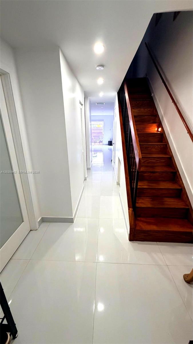 A hallway with white tile floors leads to a glass door, featuring a wooden staircase — 401 SW 109th Ave # 14, Miami FL 33174, MIAMI, FL