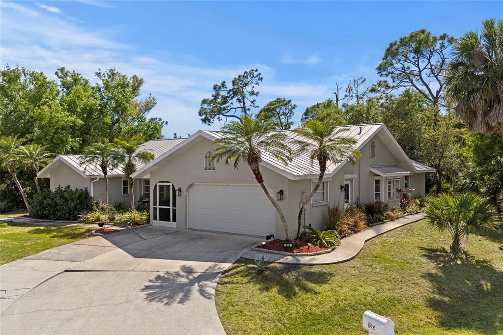 A single-story house with a metal roof, two-car garage, and palm trees in the yard — 935 BAER AVENUE NW, PORT CHARLOTTE, FL