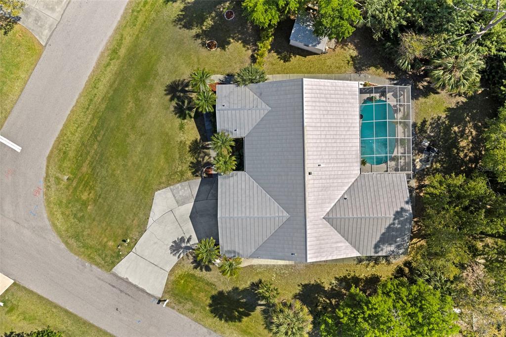 An aerial view shows a house with a metal roof, a screened pool, and driveway — 935 BAER AVENUE NW, PORT CHARLOTTE, FL