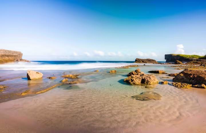 A rocky beach with shallow tide pools and ocean waves under a clear blue sky — PR 681 KM 11.7 ISLOTE WARD, ARECIBO, PR