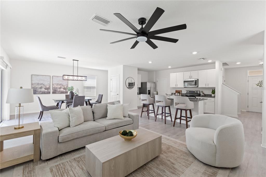 An open-concept living room and kitchen feature light wood floors, white cabinetry, and a ceiling fan — 10823 TRAILING VINE DRIVE, TAMPA, FL