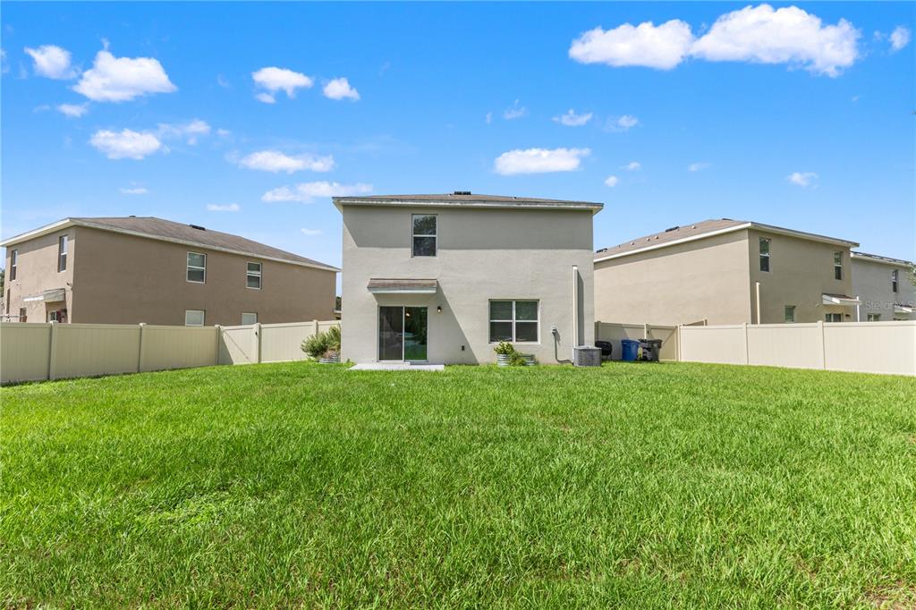 The exterior rear view of a two-story house features a grassy yard and vinyl fencing — 10823 TRAILING VINE DRIVE, TAMPA, FL