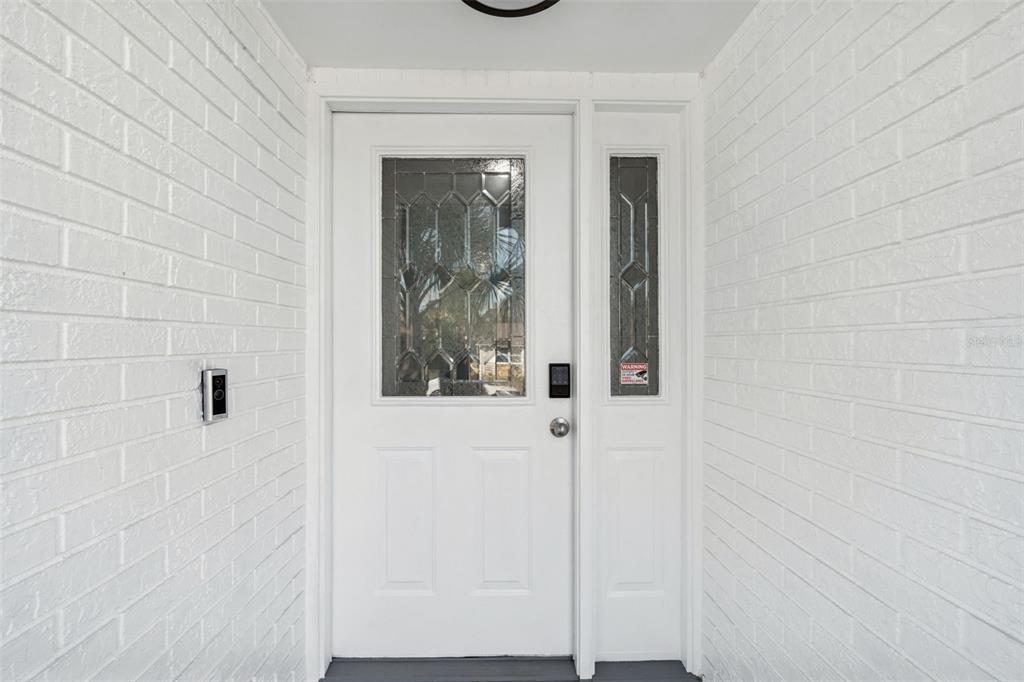 A white front door with a glass panel and sidelight is set between white brick walls — 3309 BRIARWOOD LANE, SAFETY HARBOR, FL