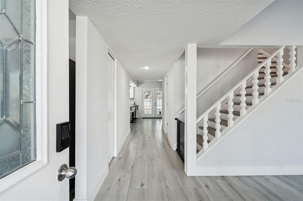 A bright entryway features light wood-look flooring, white walls, and a staircase with white railings — 3309 BRIARWOOD LANE, SAFETY HARBOR, FL