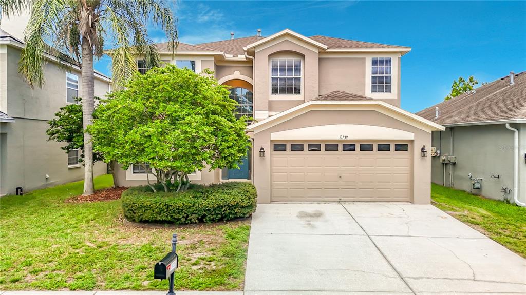 A two-story suburban house features a tan stucco exterior, a two-car garage, and landscaping — 10739 EVENINGWOOD COURT, TRINITY, FL