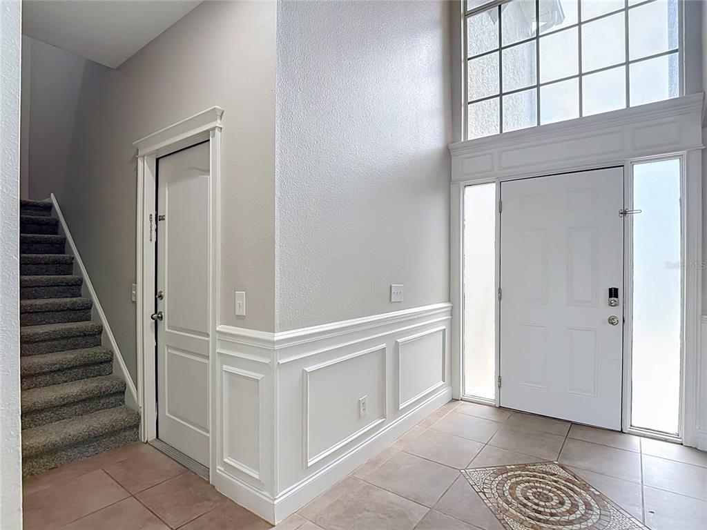 An entryway features a staircase, a white front door with sidelights, and wainscoting on walls — 10739 EVENINGWOOD COURT, TRINITY, FL